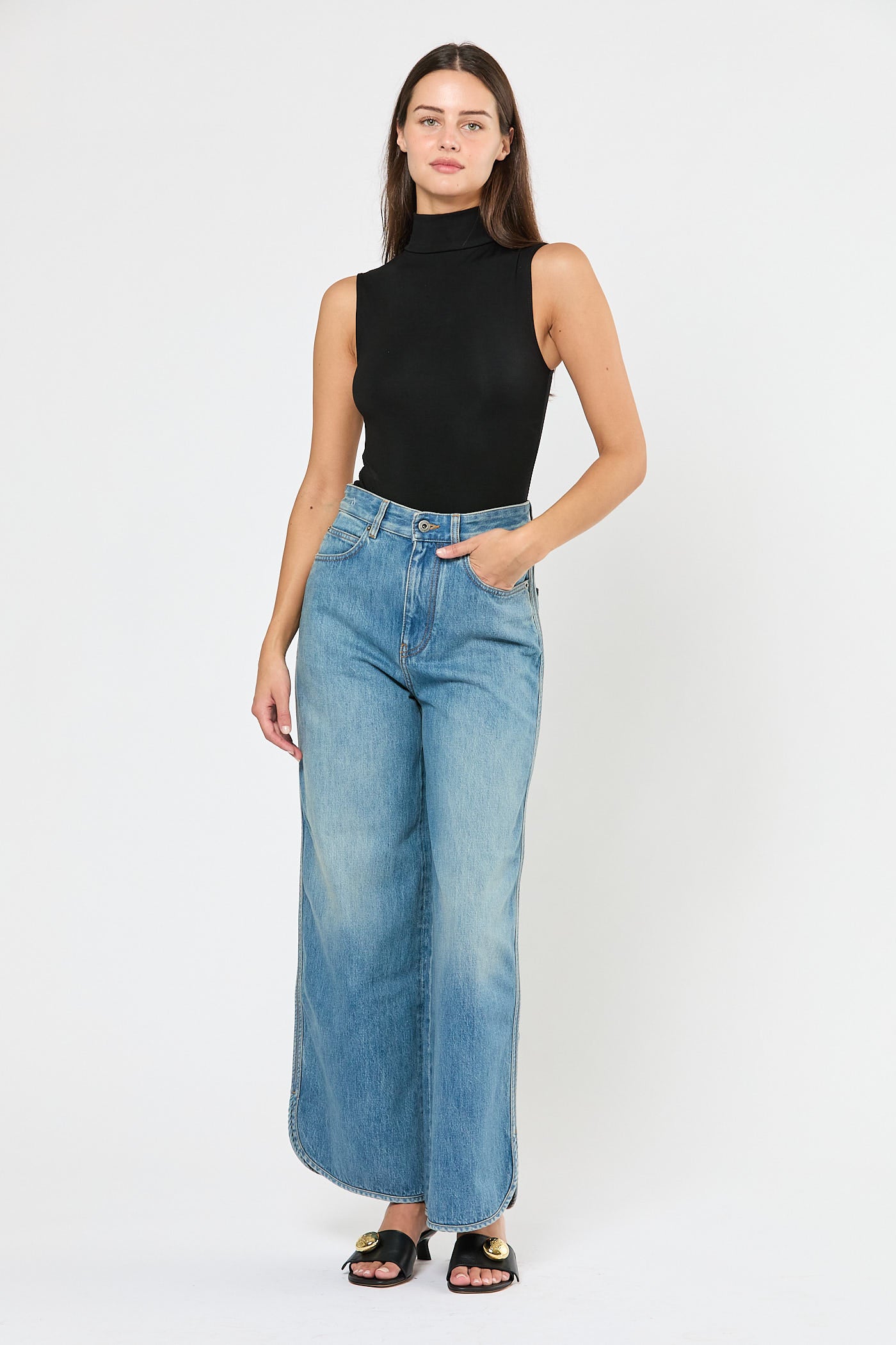 Woman wearing a black sleeveless top and light blue jeans on a white background