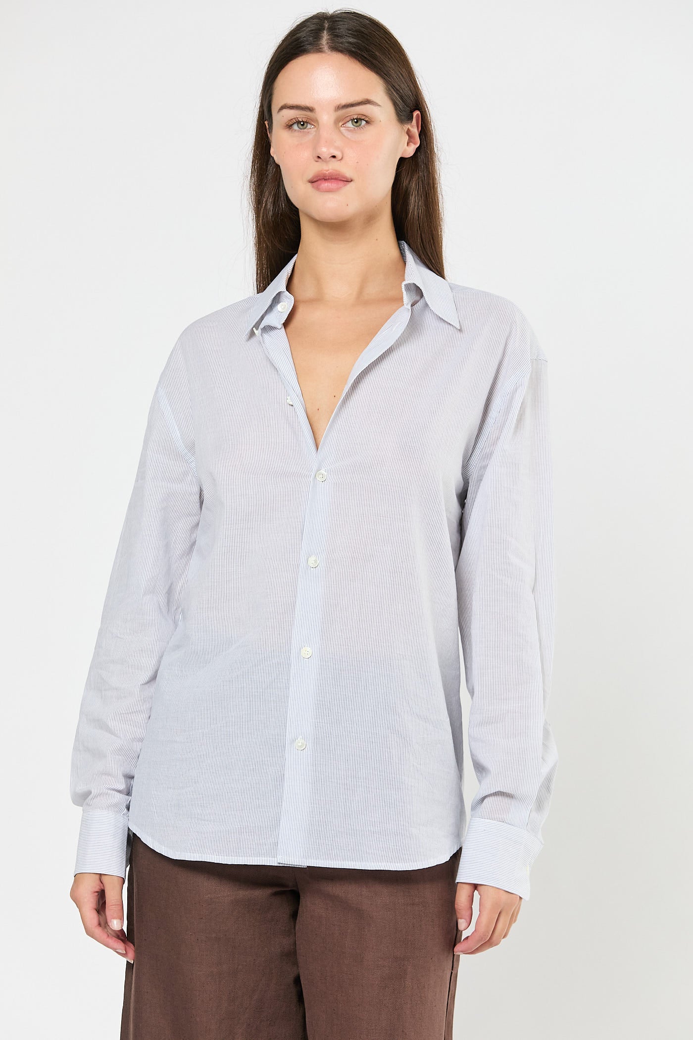 Woman wearing a striped white button-up shirt and brown pants on a white background