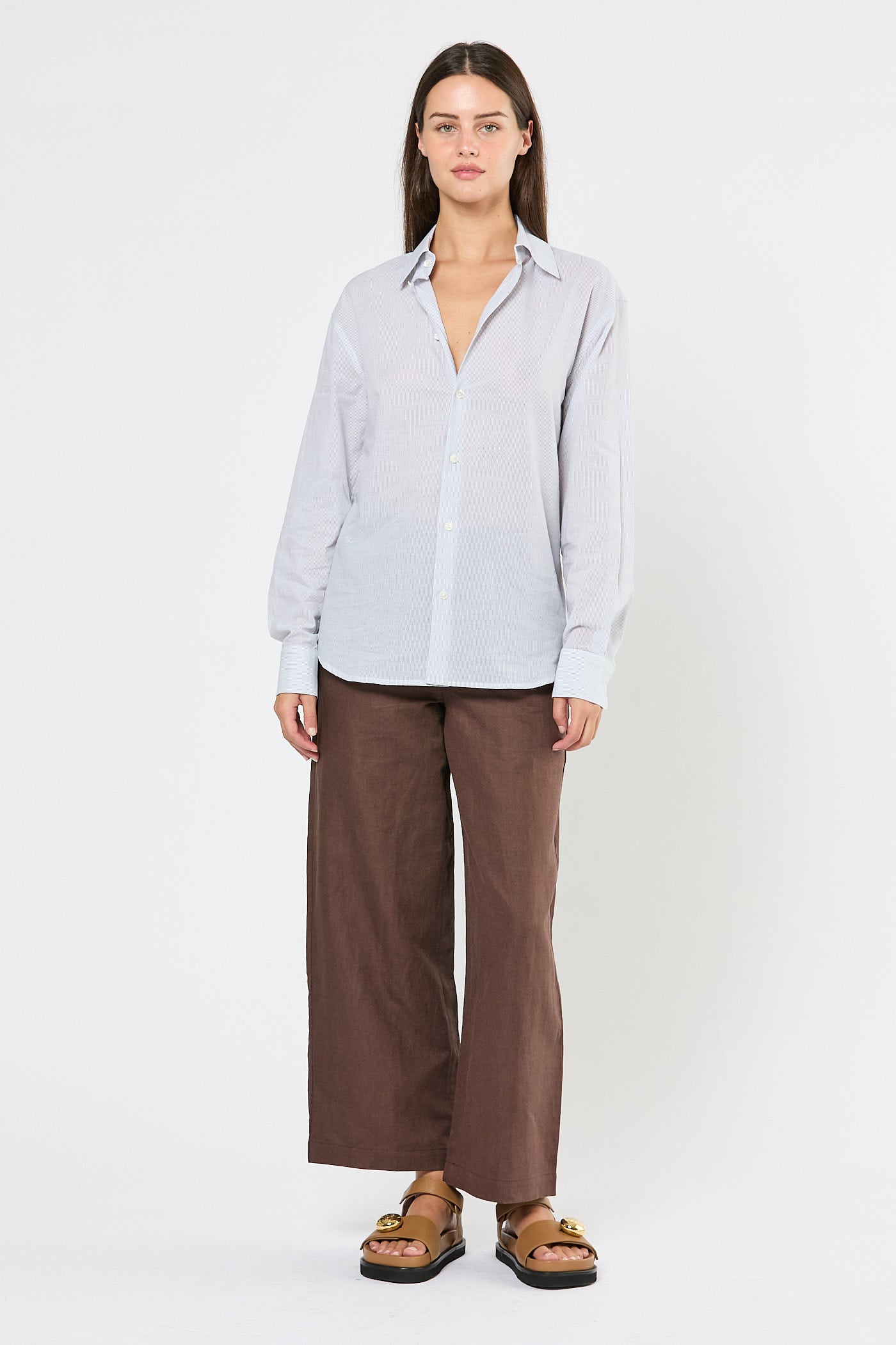 Woman wearing a striped white shirt and brown pants on a white background