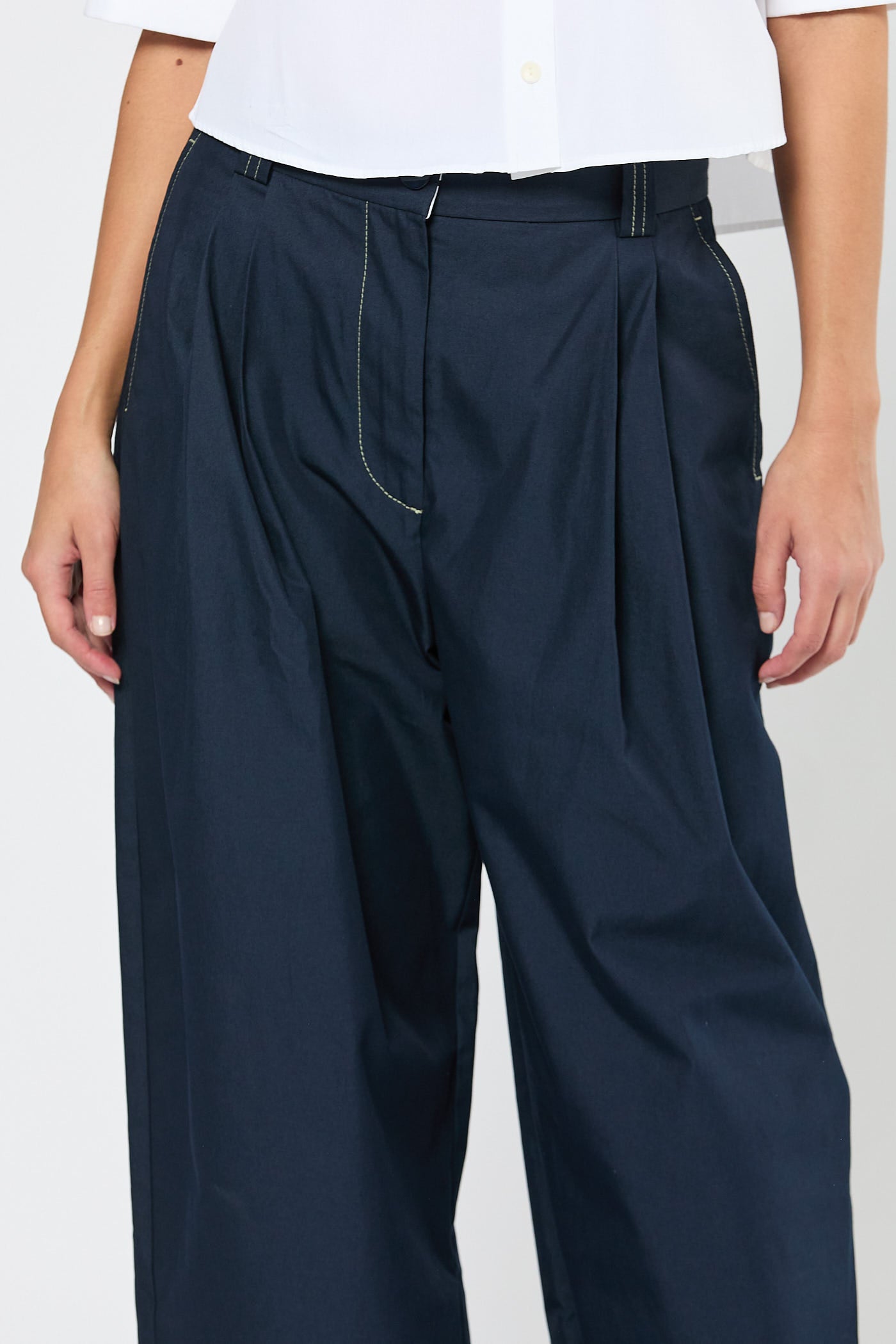 Navy pleated pants worn by a person on a white background