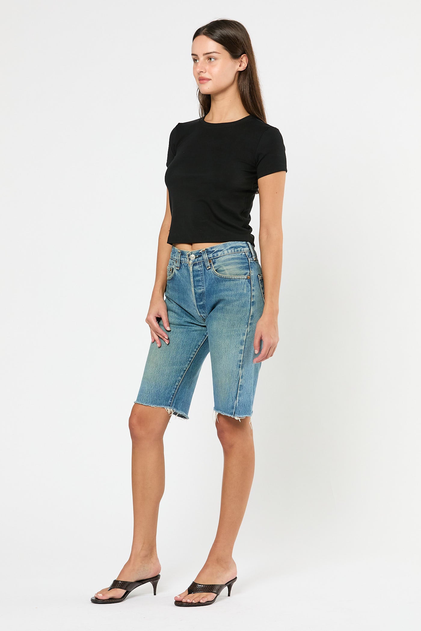 Woman wearing a black crop top and blue denim shorts on a white background