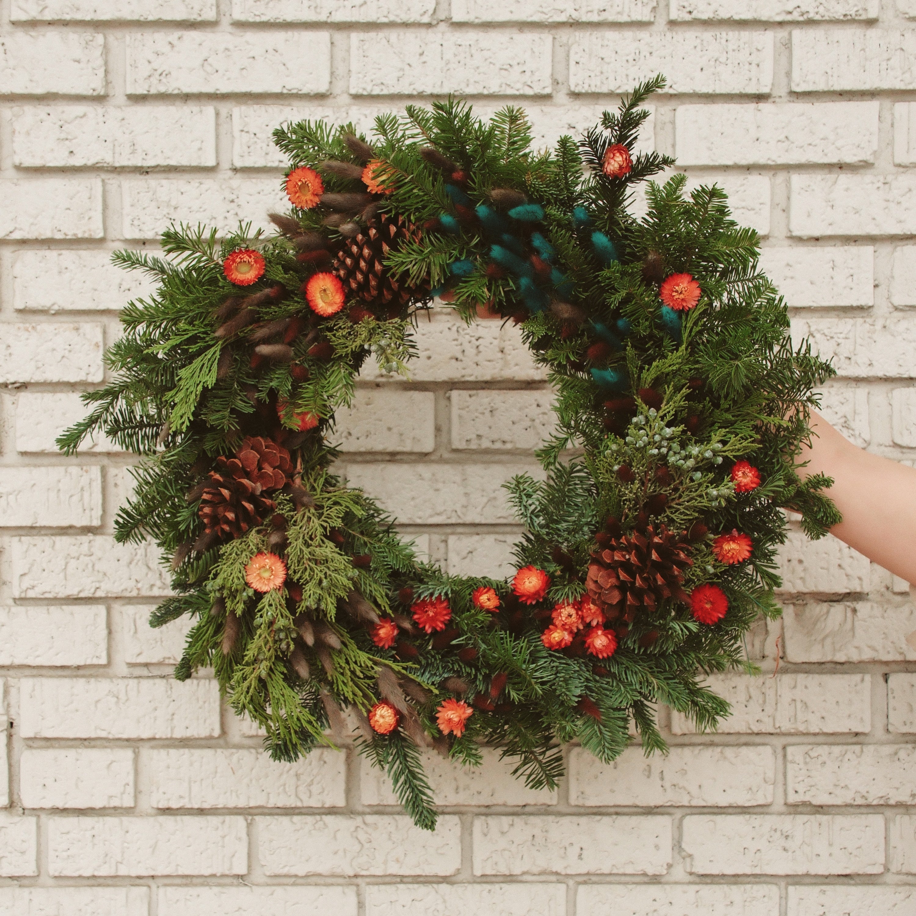 Green wreath with pinecones and berries against a light brick wall