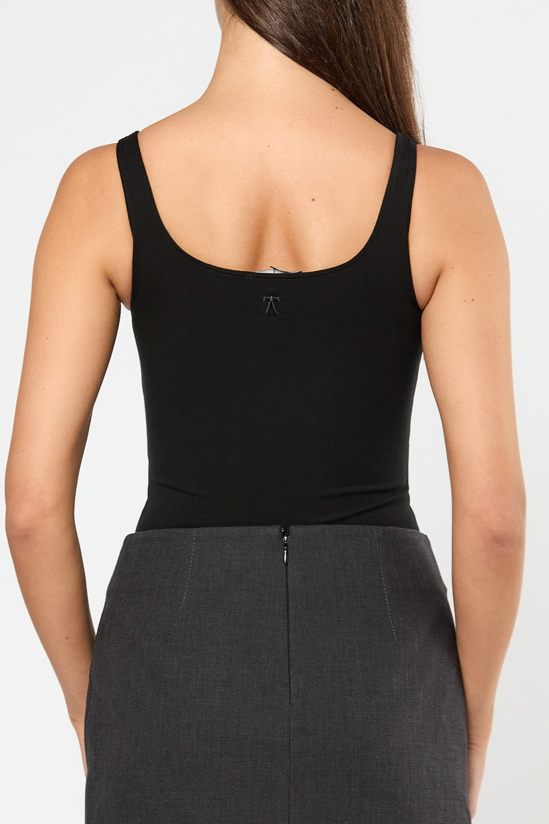 Person wearing a black tank top and gray skirt on a white background